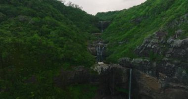 Hava görüntüsü. Yeşil ormandaki adada güzel bir şelale. Yüksek bir uçurumdan düşen su