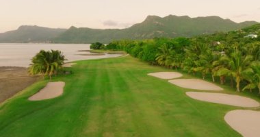 Golf oteli kıyısı Hint Okyanusu. Sahilde golf sahası ve villalar. Golf sahasının havadan görüntüsü. Atış yapmak, golf kulübünün üzerinde uçmak. Yaz zamanı, gün batımı. Zengin insanların hayatı. Mauritius.