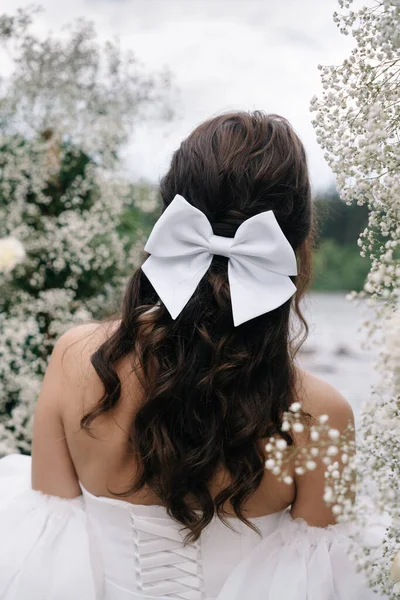 Gelinlik giymiş bir gelin ve doğadaki tören alanının arka planında bir fiyonk.