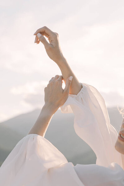 Hands of the bride in a wedding dress against the backdrop of mountains at sunset