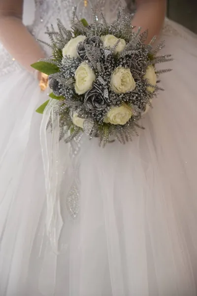 Vit hud brud i en vit bröllopsklänning med guld smycken och en bukett blommor — Stockfoto