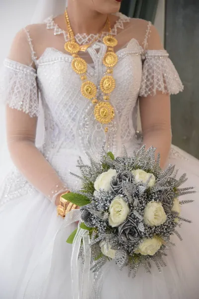 Biała panna młoda w białej sukni ślubnej ze złotą biżuterią i bukietem kwiatów — Zdjęcie stockowe