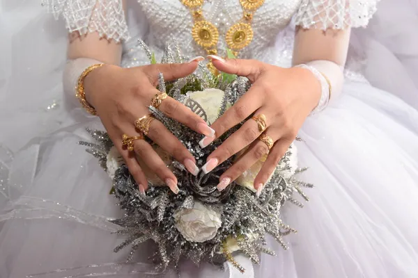Sposa dalla pelle bianca in un abito da sposa bianco con gioielli in oro e un mazzo di fiori — Foto Stock