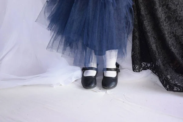 Τα πόδια ενός μικρού κοριτσιού με μαύρα παπούτσια και λευκό καλσόν, το στρίφωμα ενός μπλε δαντελένιου φορέματος, στέκεται κοντά στη νύφη — Φωτογραφία Αρχείου