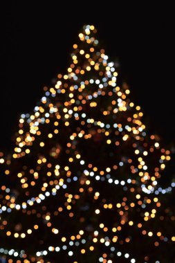 Siyah arka planda Noel ağacı ışıkları. Doğal, neşeli Bokeh ışıklandırması. Mutlu yıllar ve kış tatilleri tebrik kartı konsepti. Şehirdeki açık hava Xmas Fuarı. Odaklanmamış