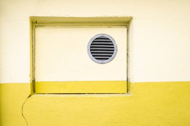Ventilation grill in yellow house wall. Old building air condition. Painted stone and concrete wall background. Housing facilities. Copy space