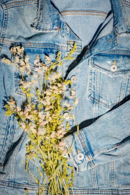 Çiçekli mavi kot pantolon. Yaratıcı bir geçmiş. Yırtık kumaş cekette sarı çayır yaprakları. Yaz, bahar, tatil ve tatil kıyafetleri konsepti. Yaz ortası kutlamaları dikey arkaplan