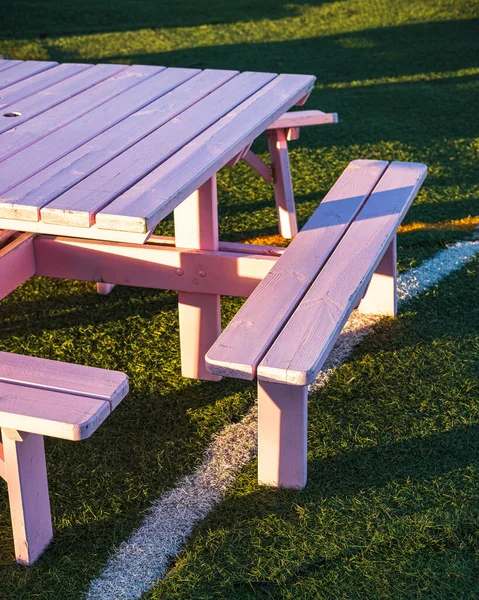 Summer picnic. Pink wooden table and chairs on green grass. Creative outdoor furniture on tennis court. Evening sunshine in the garden. Sport, activities, food delivery, family, friends time concept