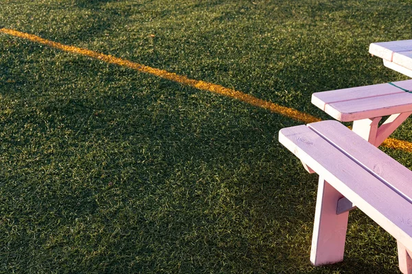 Summer picnic. Pink wooden table and chairs on green grass. Creative outdoor furniture on tennis court. Evening sunshine in the garden. Sport, activities, food delivery, family, friends time concept