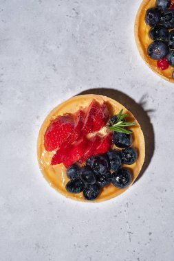 Gri taşlı arka planda meyveli kek. Kremalı, jöleli, taze çilekli ve böğürtlenli turtalar. Lezzetli fırın tatlıları. Dikey, kapat, tasarım için alanı kopyala