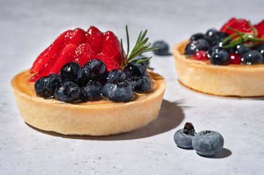 Gri taşlı arka planda meyveli kek. Kremalı, jöleli, taze çilekli ve böğürtlenli turtalar. Lezzetli fırın tatlıları. Kapatın, tasarım için alanı kopyalayın