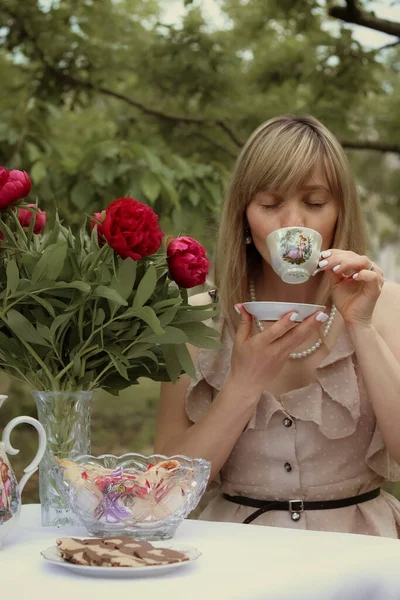 Çay içen bir kız ve yanında bir buket şakayık.