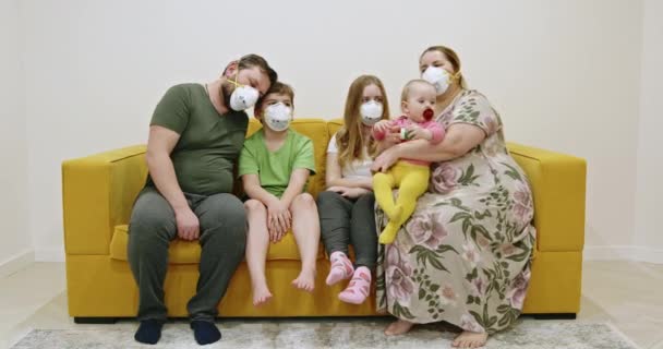 ソファに座ってマスクの家族 重い母親と父親で医療マスク巨大子供とスタッキング手一緒に座っている間に黄色のソファに自宅で検疫 — ストック動画