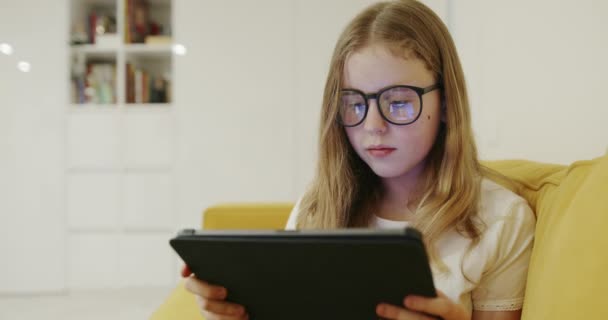 Menina Inteligente Óculos Sentados Sofá Jogando Jogo Tablet Enquanto Passa — Vídeo de Stock