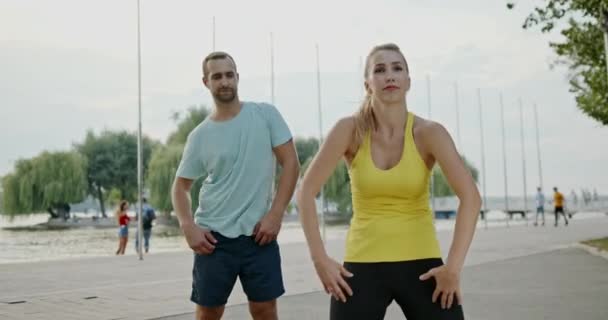 健康とフィットネスのコンセプトで彼らの筋肉をトーンするためにストレッチ体の真ん中を行う遊歩道で屋外で運動若いカップル — ストック動画