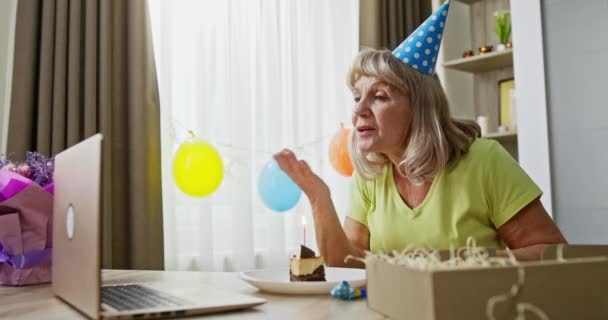 老年妇女在网上庆祝生日 在遥远的生日庆祝活动中 老妇人在网上与朋友交谈 并在蛋糕上放蜡烛 — 图库视频影像