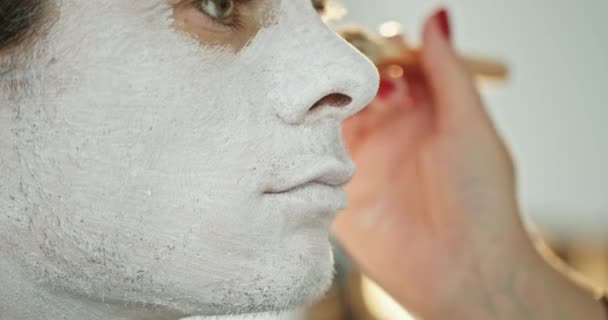 在准备万圣节庆祝活动时 作物化妆师用刷子在男模的脸上涂上白色颜料 — 图库视频影像