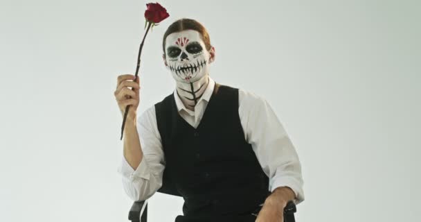 Молодой Мужчина Скелетоном Рассматривает Цветок Кладет Красную Розу Рот Сидя — стоковое видео