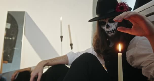 ハロウィンのお祝い中にろうそくの火に触れる怖いメイクの若い男 — ストック動画