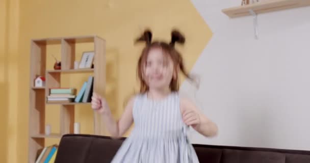 Podekscytowana Dziewczynka Kratkę Sukienka Uśmiecha Się Skacze Kanapie Podczas Zabawy — Wideo stockowe