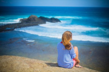 Kız sahilde oturuyor.