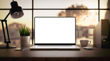 Laptop with blank screen on table in livingroom during golden sunset or sunrise - home office background