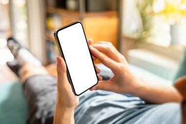 Evdeki koltukta yatarken akıllı telefon boş ekran çerçevesiz modern tasarım kullanan bir adam.
