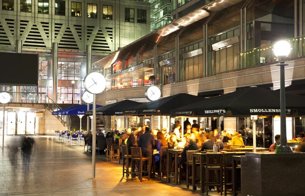 LONDRES, CANARIO WHARF UK - 4 DE ABRIL DE 2014 Vista cuadrada de Canary Wharf con luces nocturnas y trabajadores de oficina relajados después de la jornada laboral en cafeterías y pubs locales — Foto de Stock