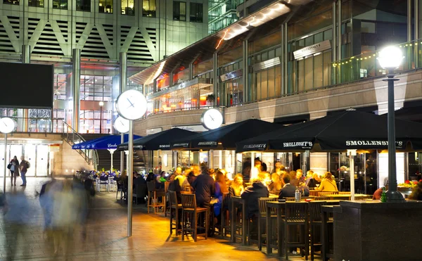 LONDRES, CANARIO WHARF UK - 4 DE ABRIL DE 2014 Vista cuadrada de Canary Wharf con luces nocturnas y trabajadores de oficina relajados después de la jornada laboral en cafeterías y pubs locales — Foto de Stock