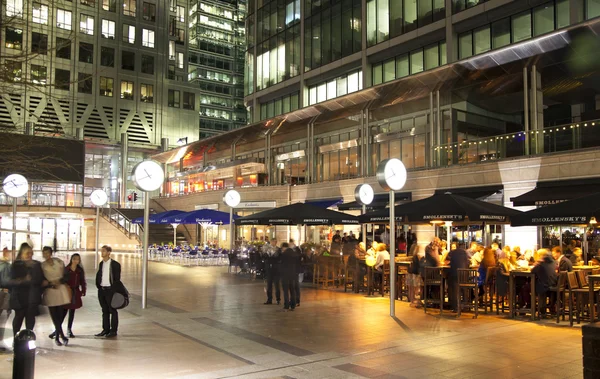 LONDRES, CANARIO WHARF UK - 4 DE ABRIL DE 2014 Vista cuadrada de Canary Wharf con luces nocturnas y trabajadores de oficina relajados después de la jornada laboral en cafeterías y pubs locales — Foto de Stock