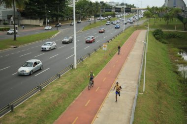 Salvador, Bahia, Brezilya - 30 Eylül 2021: Salvador 'da bir araç yolunun yanında bisiklet yolu üzerinde seyahat eden bisikletçi.