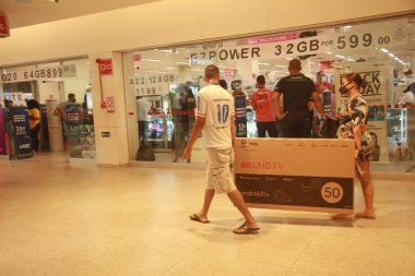 Salvador, Bahia, Brezilya - 26 Kasım 2021: Kara Cuma döneminde Salvador 'da bir alışveriş merkezinde satın alınmış akıllı bir TV taşıyan kişi.
