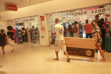 Salvador, Bahia, Brezilya - 26 Kasım 2021: Kara Cuma döneminde Salvador 'da bir alışveriş merkezinde satın alınmış akıllı bir TV taşıyan kişi.