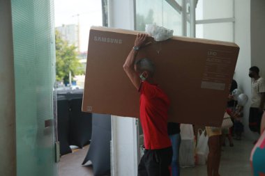 Salvador, Bahia, Brezilya - 26 Kasım 2021: Kara Cuma döneminde Salvador 'da bir alışveriş merkezinde satın alınmış akıllı bir TV taşıyan kişi.
