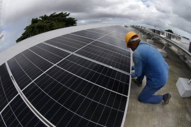 Salvador, Bahia, Brezilya - Haziran 6, 2022: Salvador şehrindeki bir devlet okulunun çatısında güneş enerjisi üretim panelleri ile çalışan işçi.