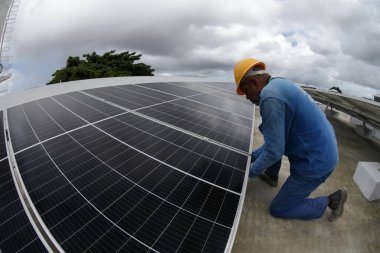Salvador, Bahia, Brezilya - Haziran 6, 2022: Salvador şehrindeki bir devlet okulunun çatısında güneş enerjisi üretim panelleri ile çalışan işçi.