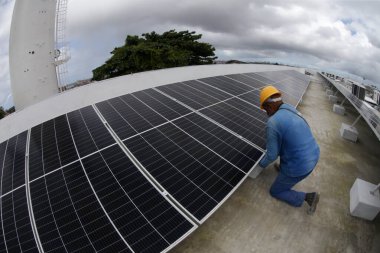 Salvador, Bahia, Brezilya - Haziran 6, 2022: Salvador şehrindeki bir devlet okulunun çatısında güneş enerjisi üretim panelleri ile çalışan işçi.