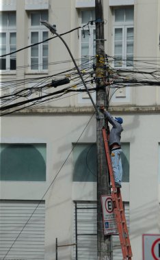 Salvador, Bahia, Brezilya - 20 Haziran 2022: Merdivendeki adam Salvador şehrindeki elektrik direğine kablo döşedi.