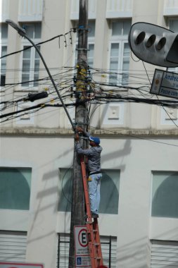 Salvador, Bahia, Brezilya - 20 Haziran 2022: Merdivendeki adam Salvador şehrindeki elektrik direğine kablo döşedi.