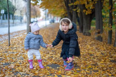 Plastik çizmeli çocuklar sonbahar parkında yapraklarla dolu patikada oynuyorlar..