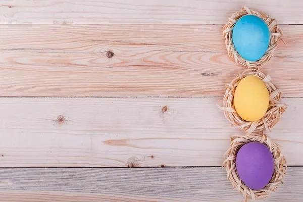 Three Easter eggs in small nests on wooden background — Stock Photo, Image