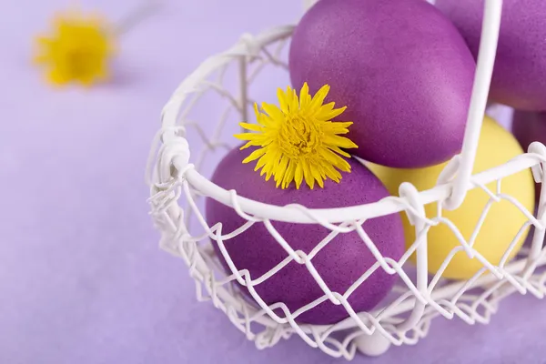 Huevos de colores en una canasta blanca sobre fondo lila —  Fotos de Stock