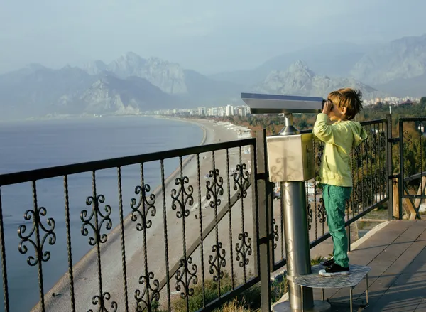 Little cute boy looking through telescope at sea viewpoint