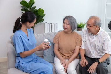 Genç hemşire bir kanepede oturan yaşlılarla ilgileniyor. Bir bayan destekçi, yaşlılara yardım ederken gülümsüyor..