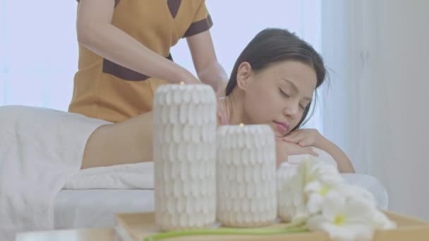 休暇中にリゾートのスパでマッサージテーブルの上に横になっている若いアジアの女性 休暇中にホテルで美肌治療中に女の子をマッサージ手 — ストック動画