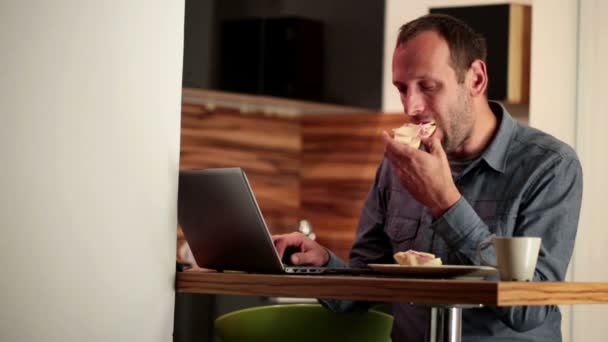 Homem trabalhando no laptop, comendo sanduíche — Vídeo de Stock