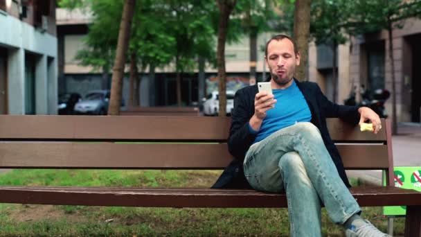 Человек ест яблоко со смартфоном — стоковое видео