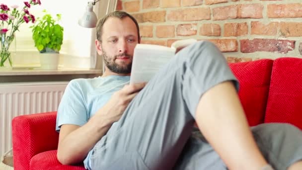 Hombre leyendo libro en sofá — Vídeos de Stock