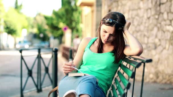 Женщина читает книгу на скамейке — стоковое видео