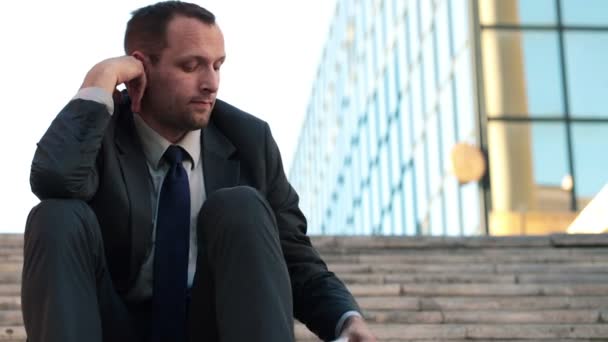 Joven hombre de negocios aburrido sentado en las escaleras de la ciudad — Vídeos de Stock